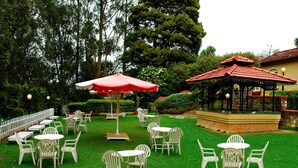 Un espace extérieur aménagé en terrasse, avec plusieurs tables et chaises, un belvédère et une clôture blanche.