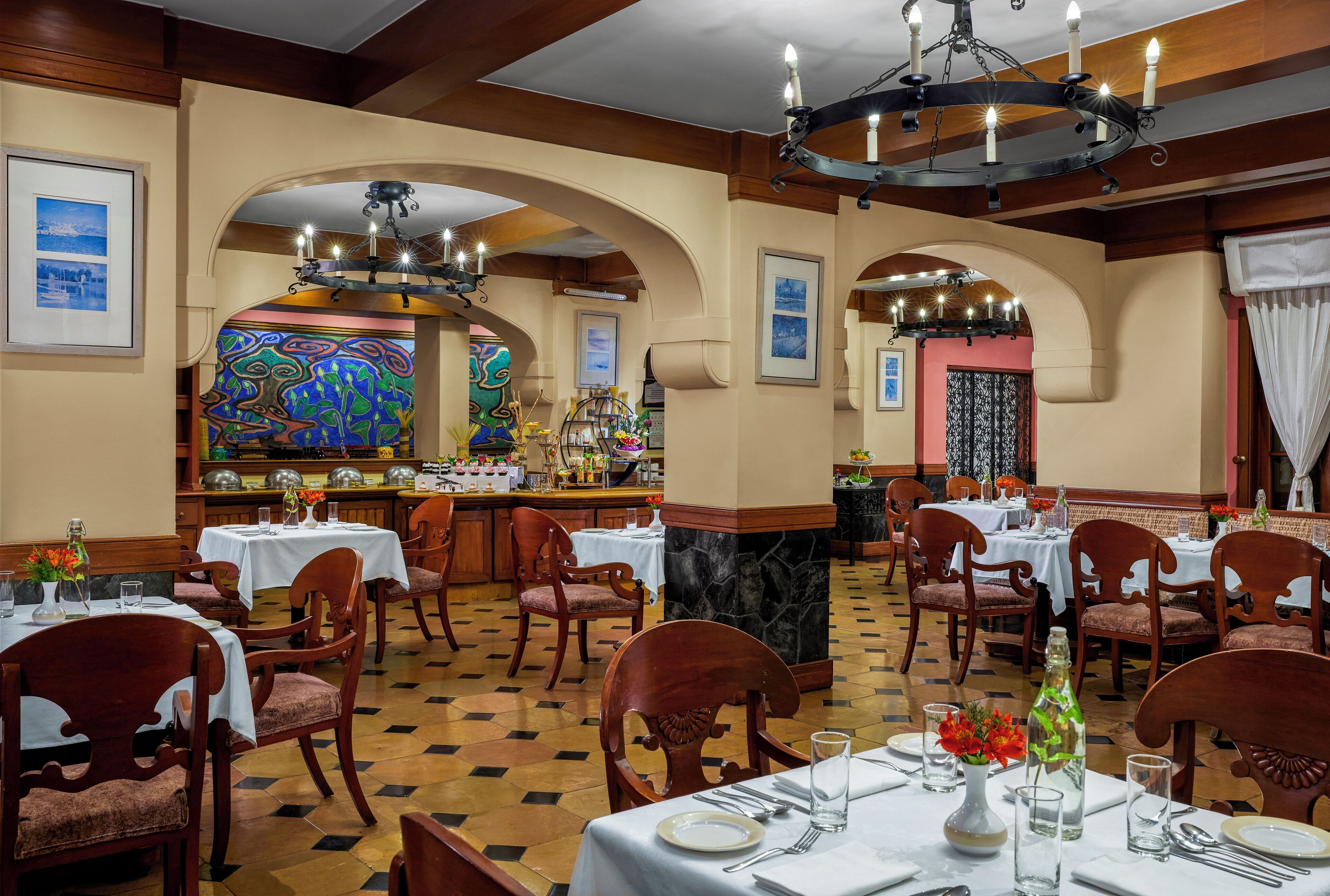A restaurant with multiple tables and chairs, a bar area, and a colorful mural on the wall.