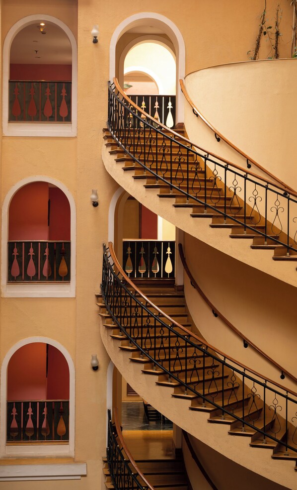 Una escalera espiral de varios niveles con barandillas negras ornamentales y barandas de madera, que conduce a varios balcones con puertas de vidrio teñidas de rojo.