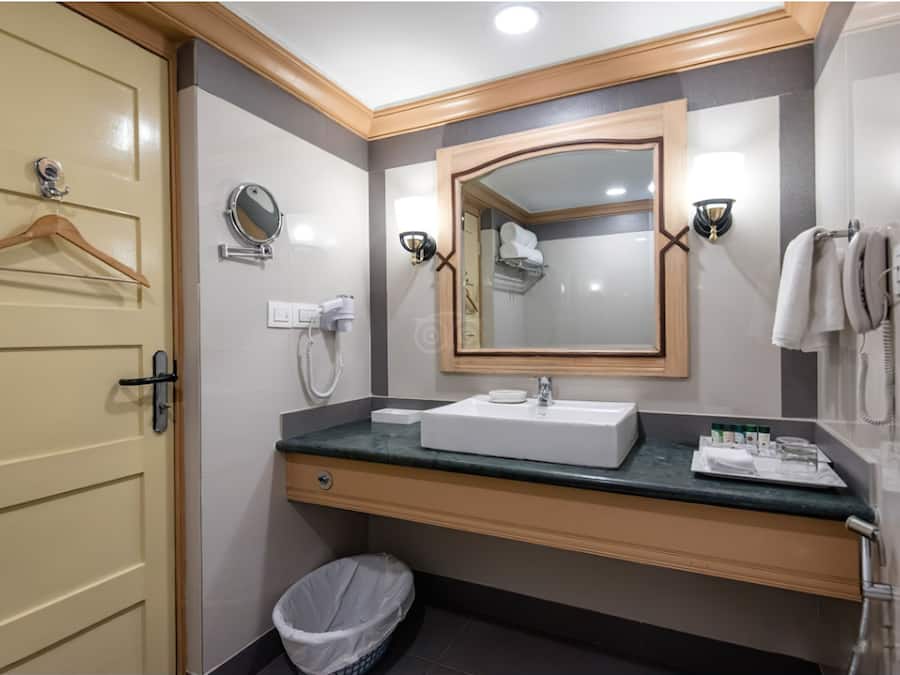 Un baño de hotel con lavamanos, espejo, toallero y una toalla colgada.