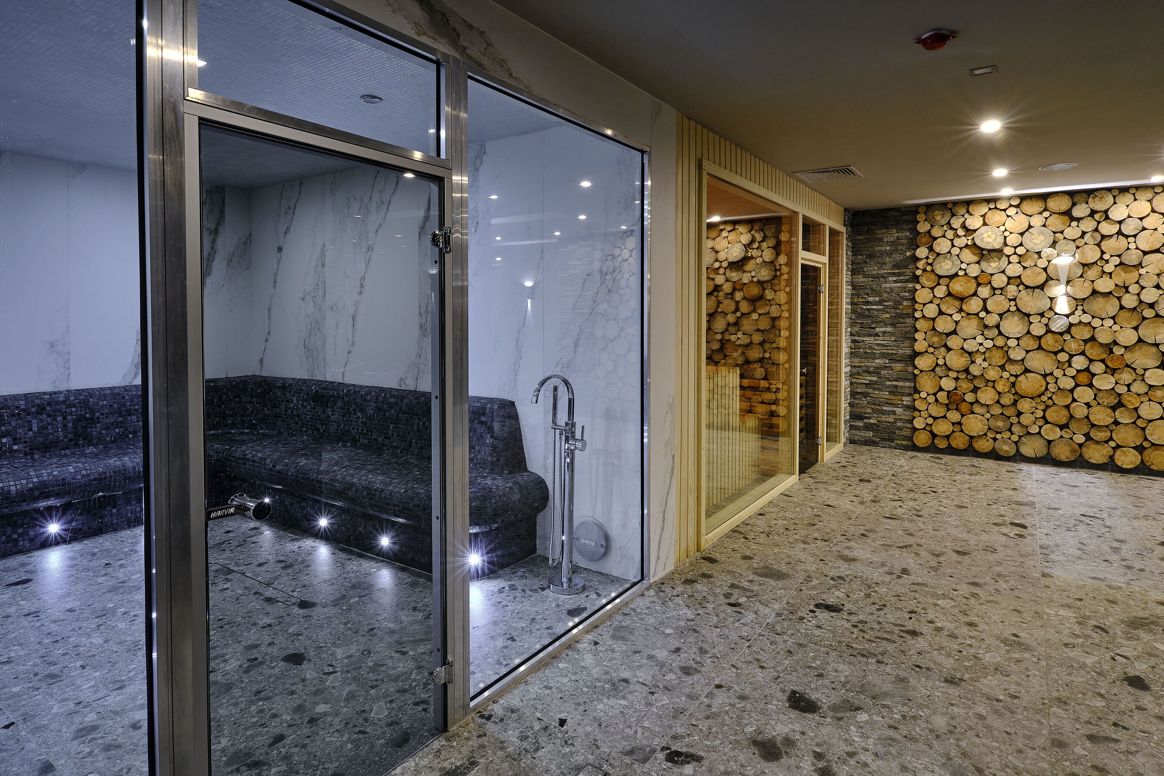Un baño moderno con ducha envuelta en vidrio, paredes de mármol y una pared de piedra con leña apilada.