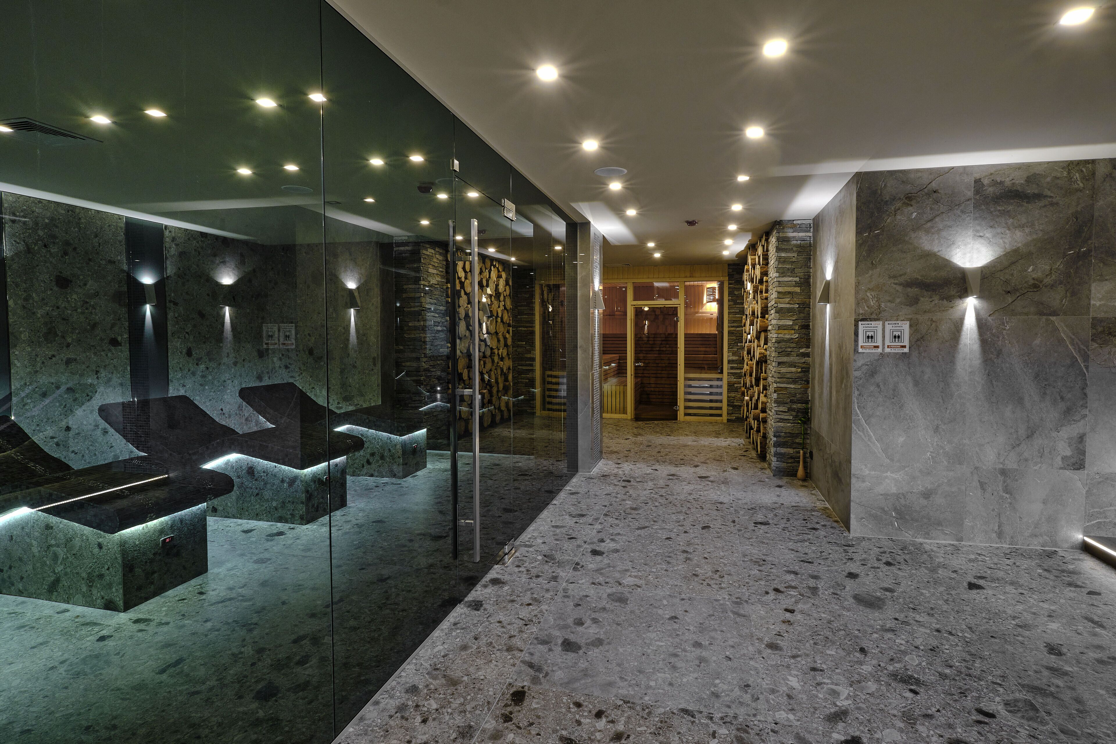 A modern bathroom with glass-enclosed sinks, a stone wall, and a marble floor.