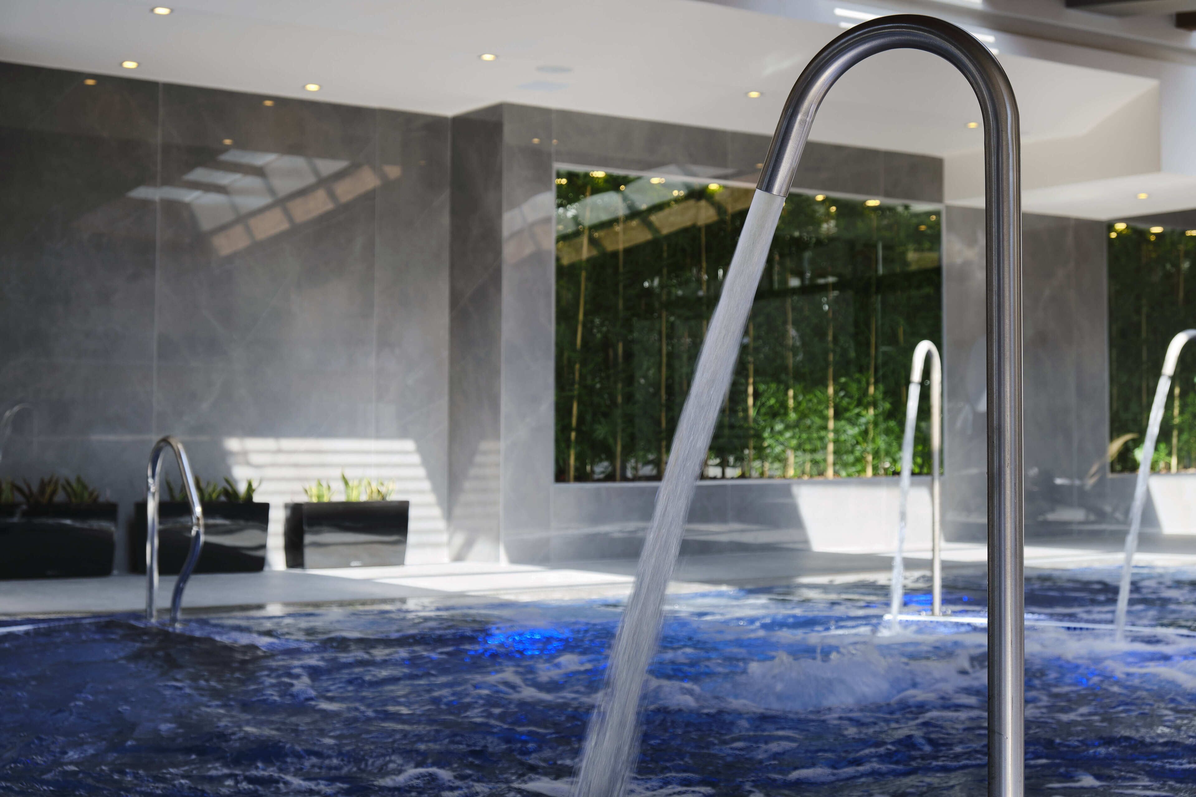 A modern indoor pool with clear water, a metal handrail, and a view of indoor plants and a large window.