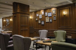 Un vestíbulo de hotel con paneles de madera, obras de arte enmarcadas en las paredes y asientos de cuero.