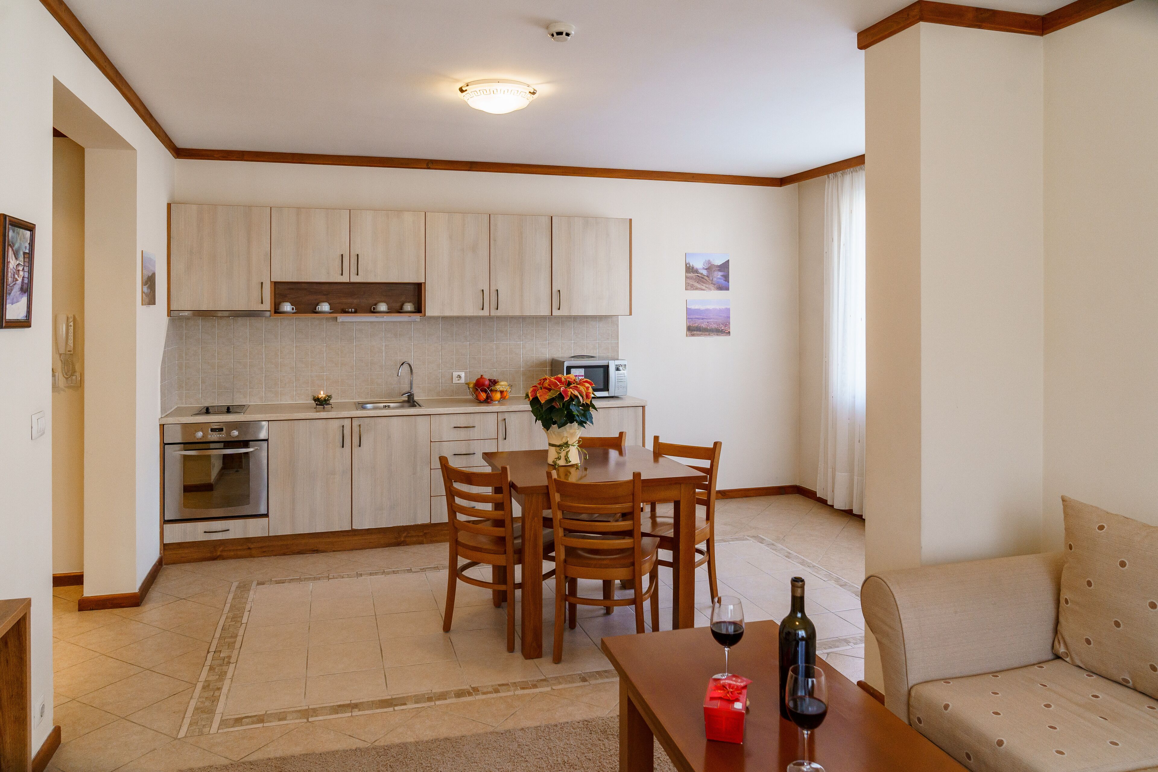 A modern kitchen with wooden cabinets, a dining table with chairs, and a sofa in a living area.