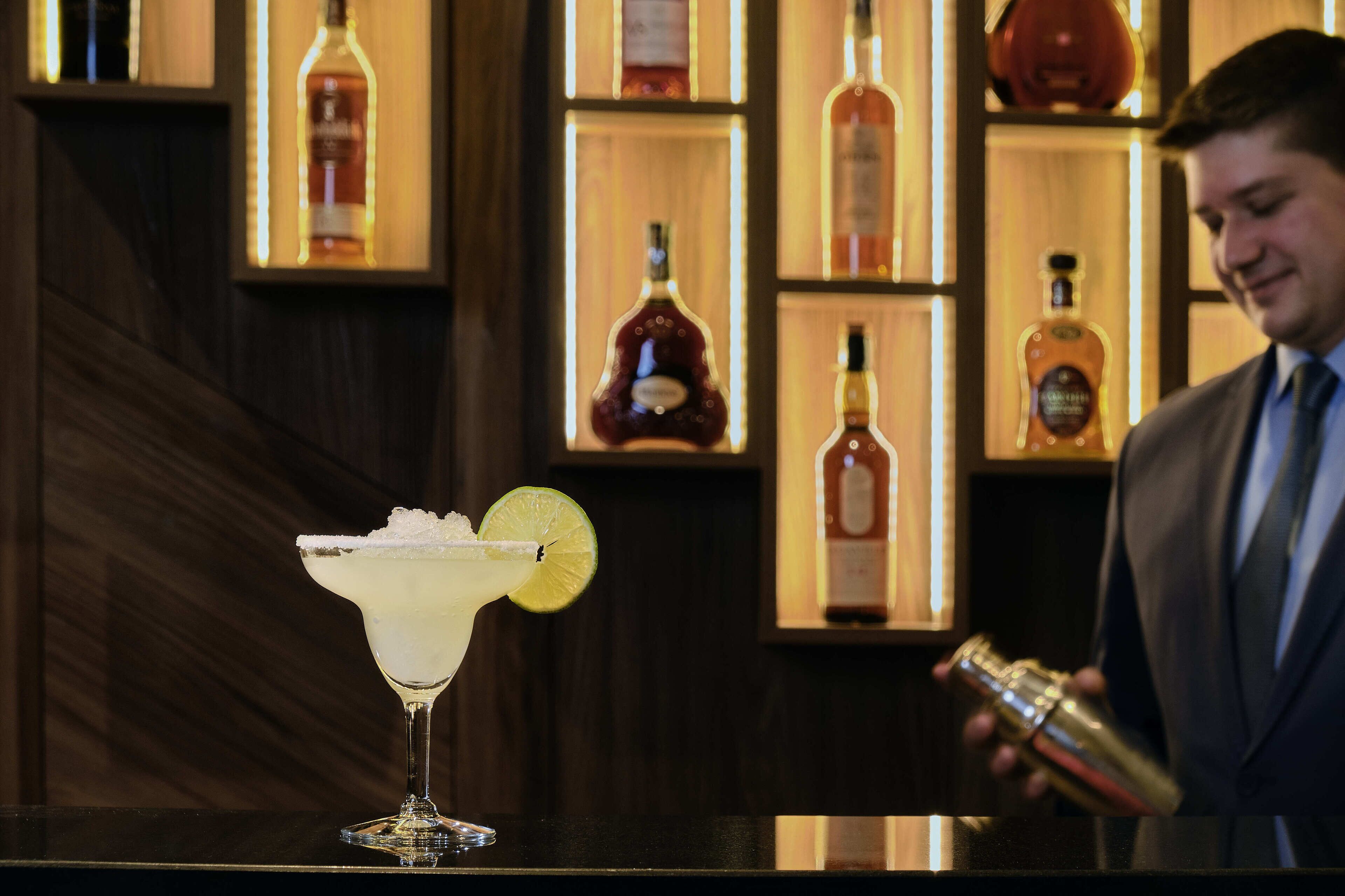 Un bar con un cóctel en la barra y una persona sirviéndolo.