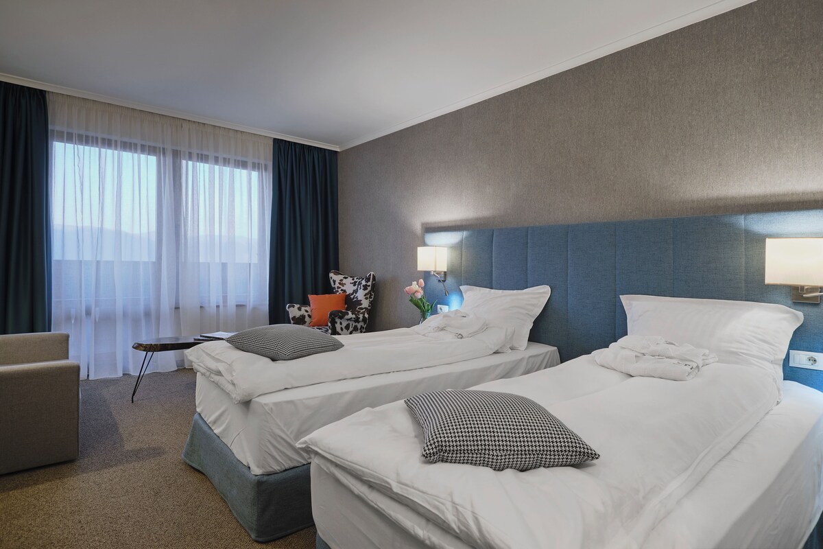 A hotel room with two beds, a sofa, a small table, and a nightstand with a lamp.