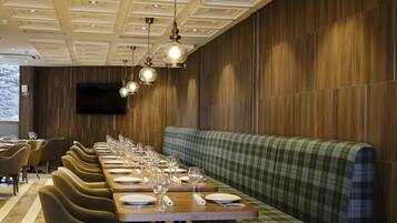 A restaurant with a long wooden table set for dining, a green plaid bench, and pendant lighting.
