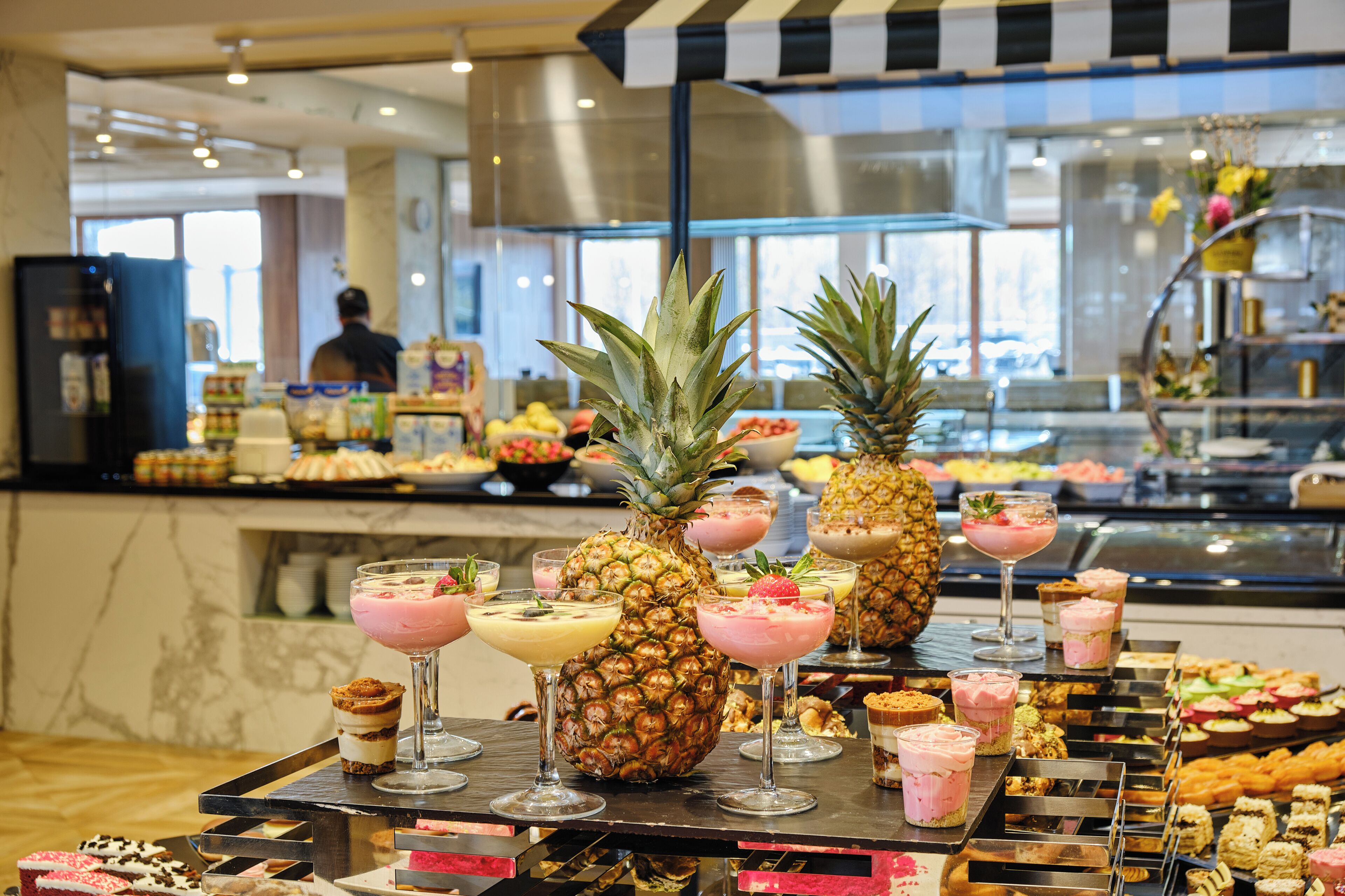 Un bufé con diversas opciones de comida y bebidas, incluyendo frutas tropicales y postres.