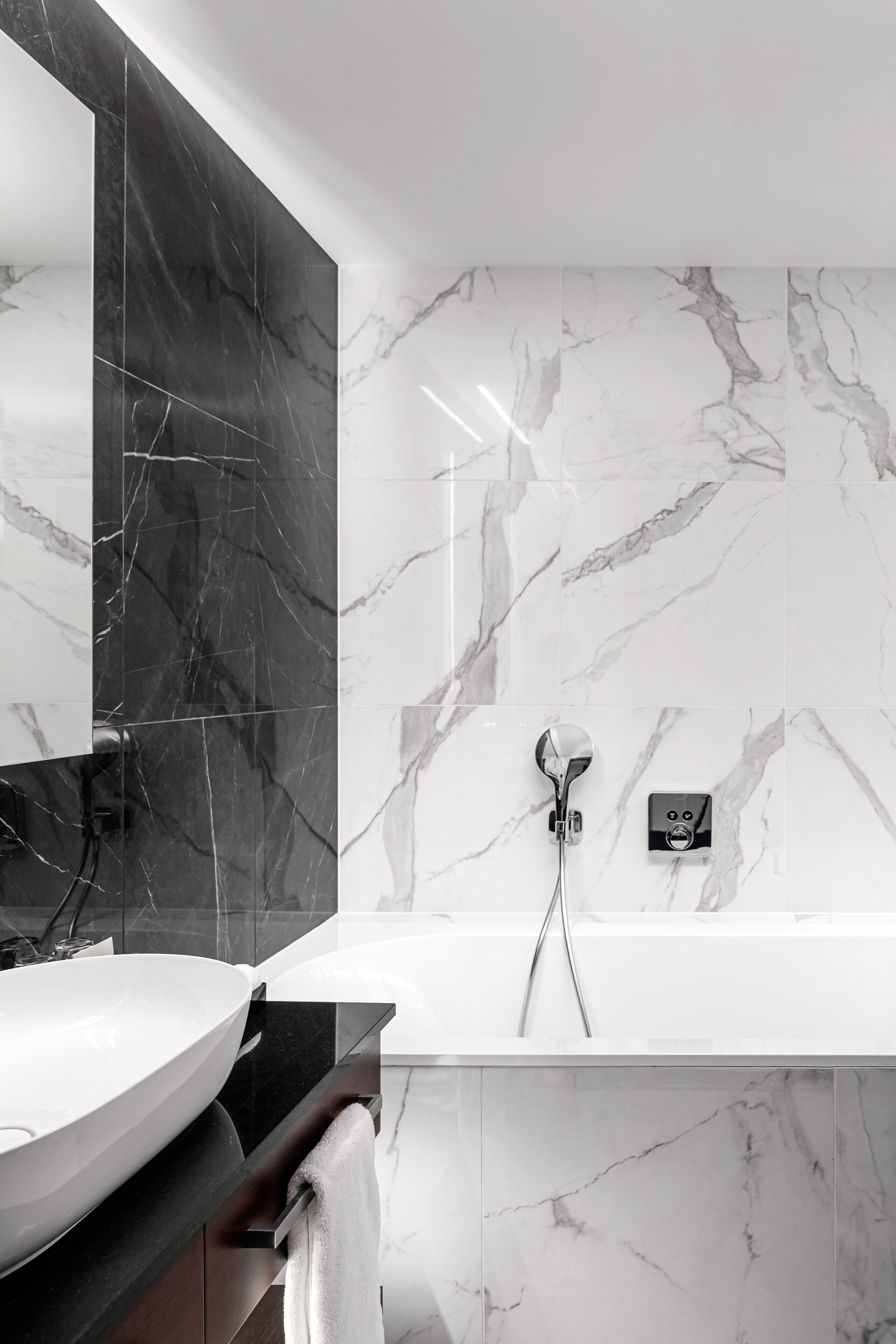 A modern bathroom with a large mirror, a vessel sink, a bathtub, and marble walls.