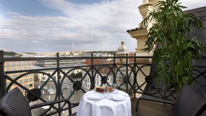 Un balcón con una mesa dispuesta para dos, con vistas a un paisaje urbano que incluye edificios y una torre.