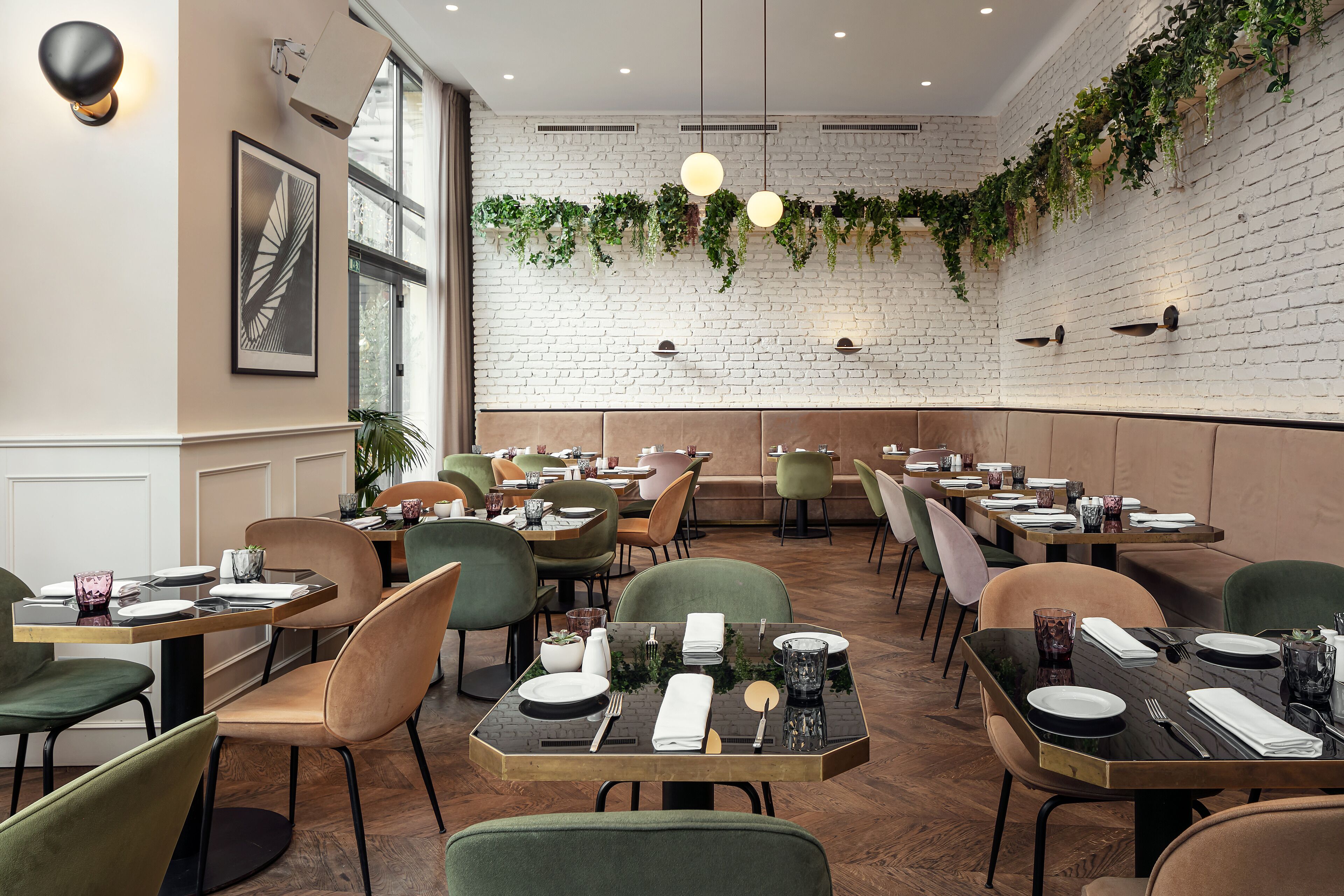A restaurant with brick walls, hanging plants, and modern lighting. Tables are set with plates, cutlery, and glasses.