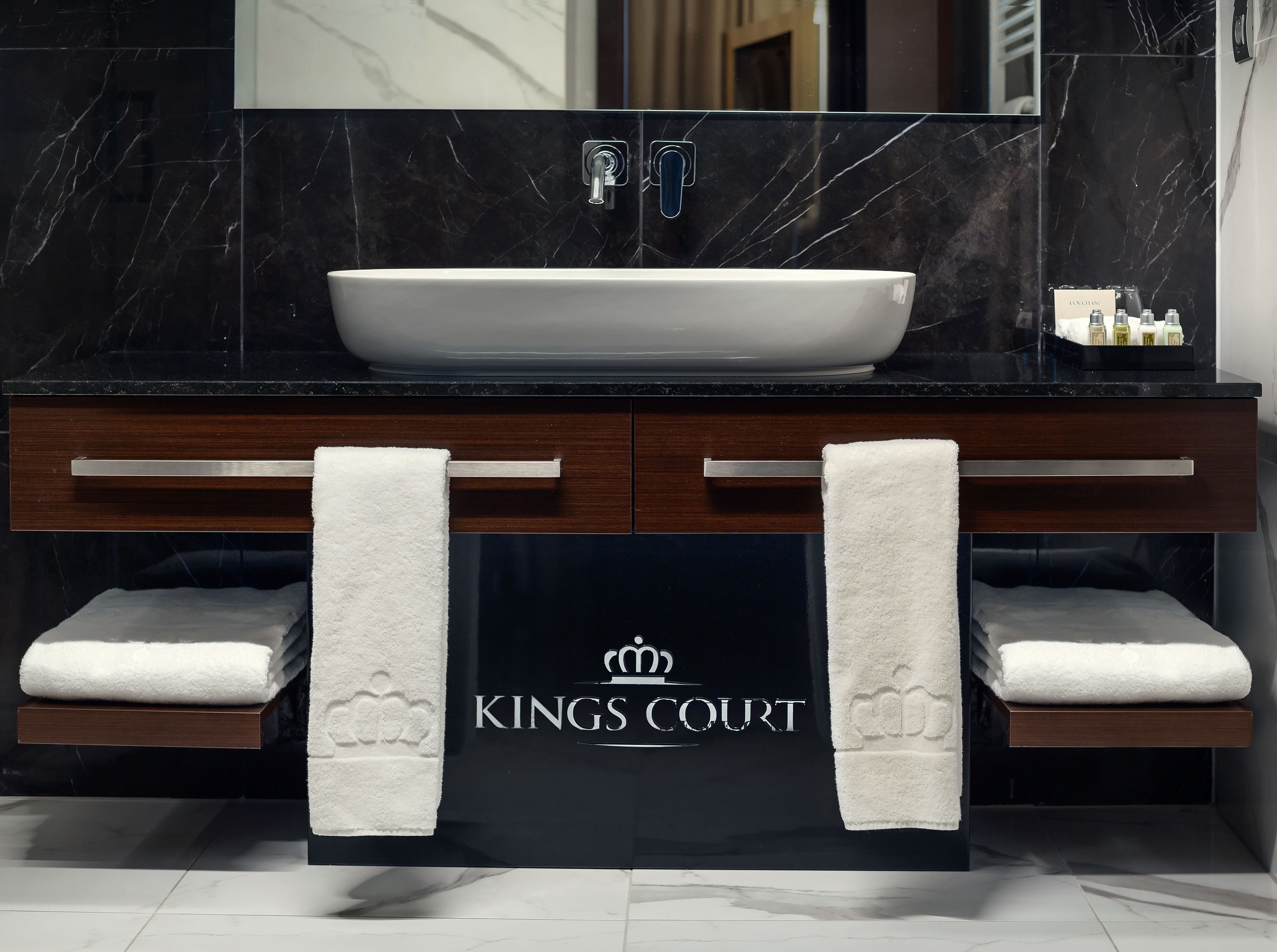 A bathroom with a black marble countertop, a white sink, and two towel racks. The towel racks have a logo that reads "KINGS COURT".