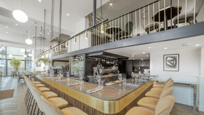 Un área de bar moderna con una barra curva, varios taburetes y una cocina al fondo.