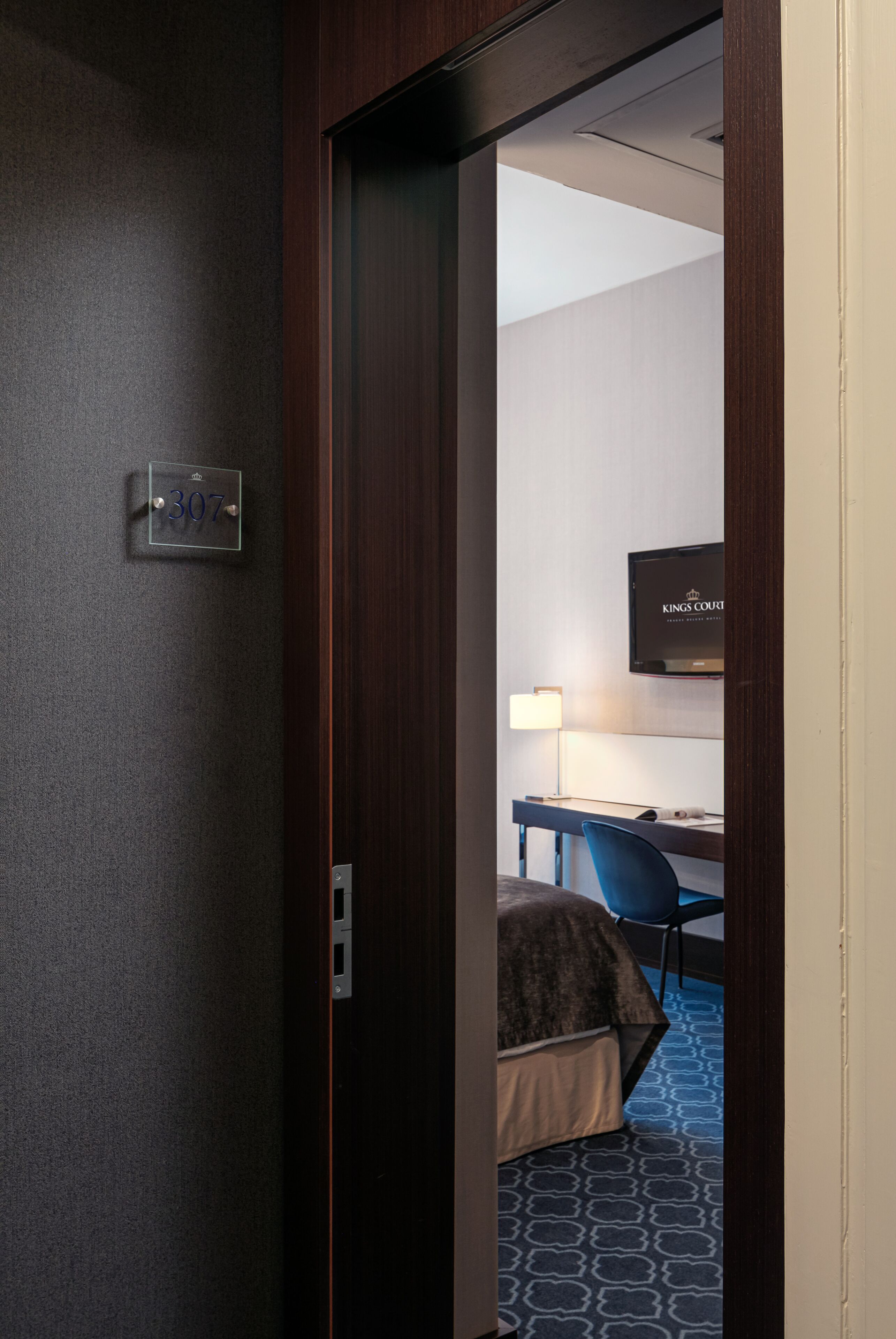 Una habitación de hotel con cama, escritorio, silla, televisor y lámpara.