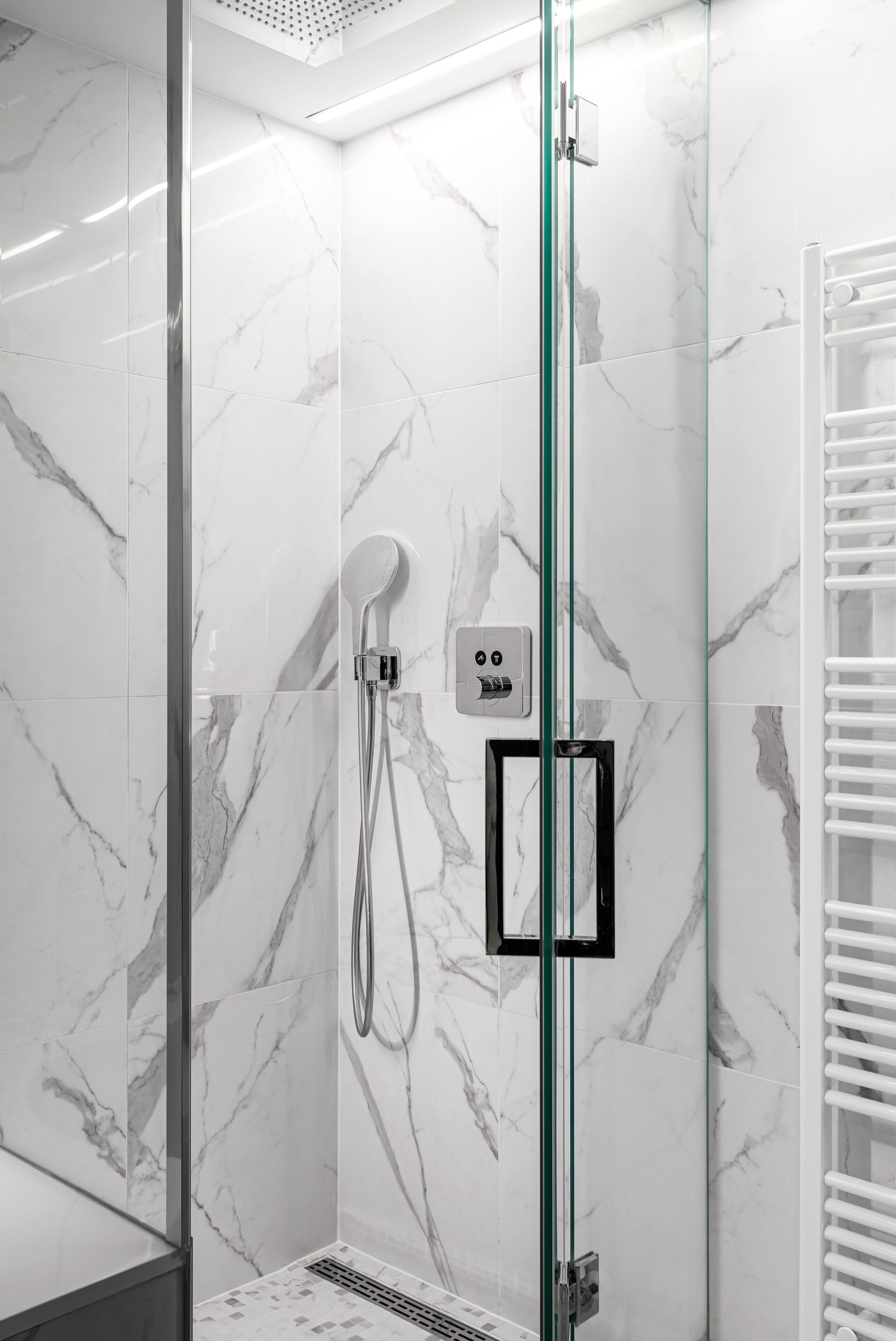 Un baño moderno con cabina de ducha de vidrio, paredes de mármol y un toallero blanco.