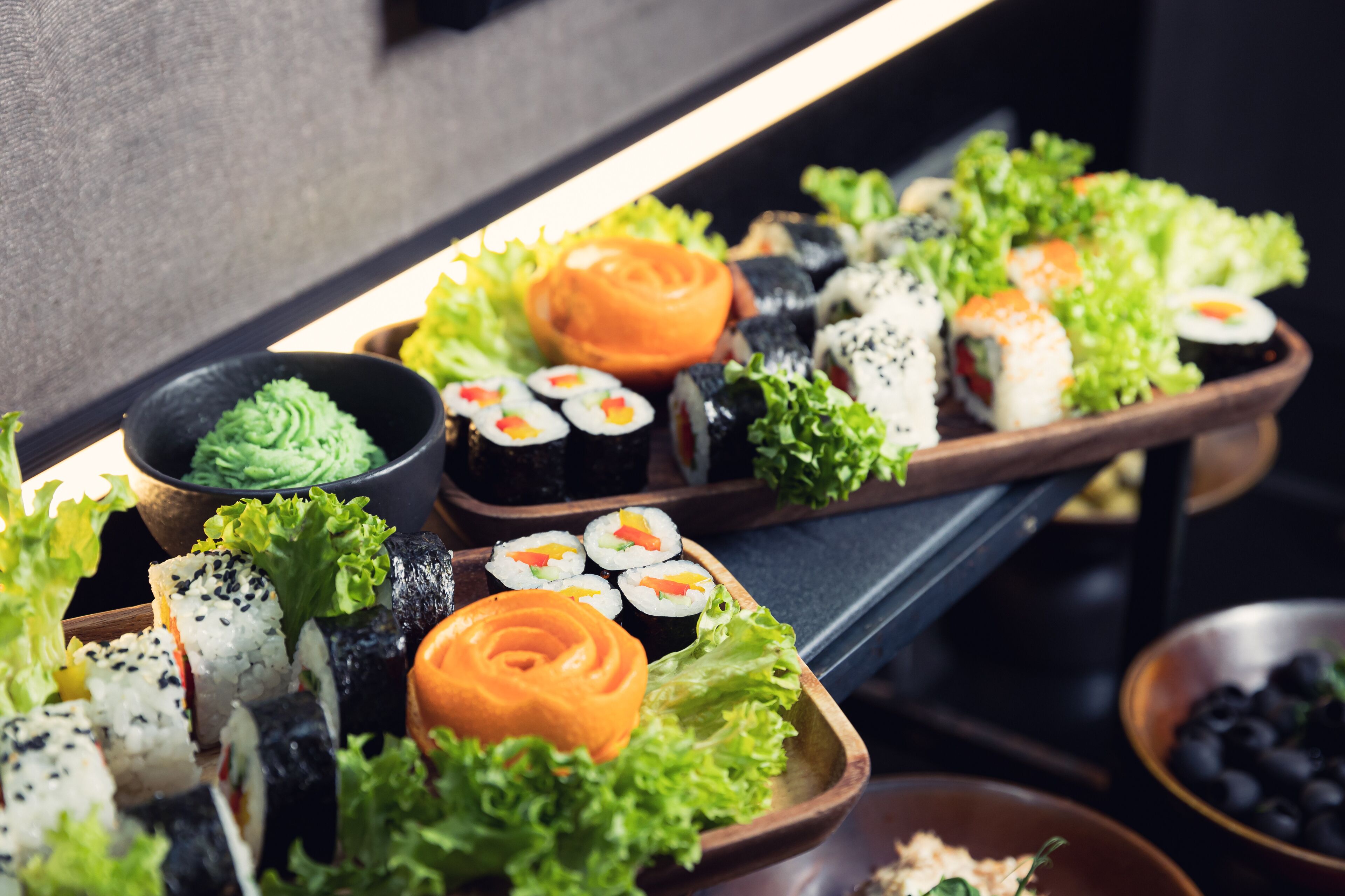 Ett urval av sushi och sashimi serverat på träbrickor med gröna salladsblad och en liten skål med sås.
