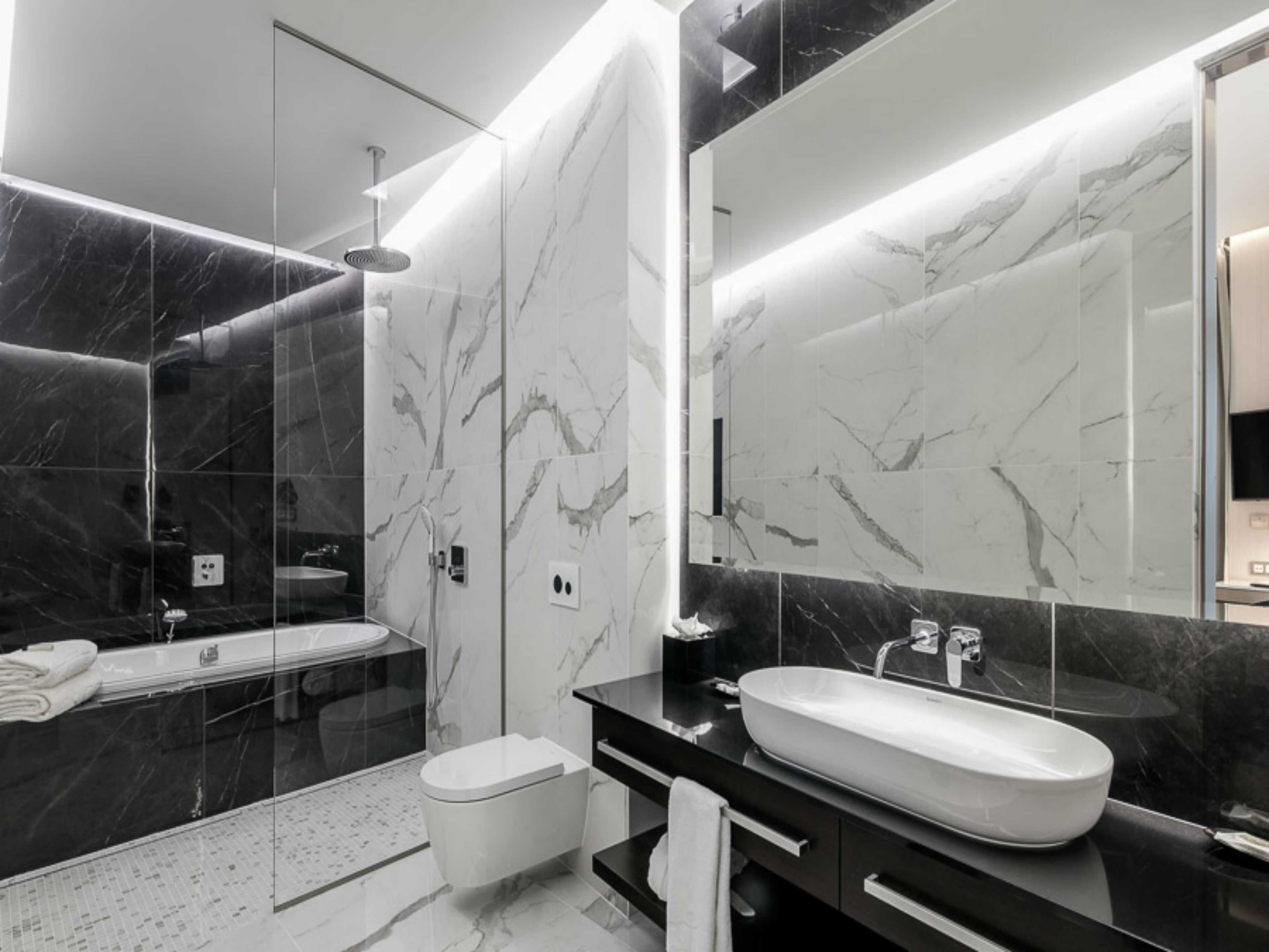 Une salle de bain moderne avec un grand miroir, une baignoire et des toilettes.