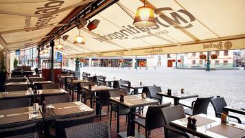 An outdoor cafe with wicker tables and chairs, a covered seating area, and a view of the street.