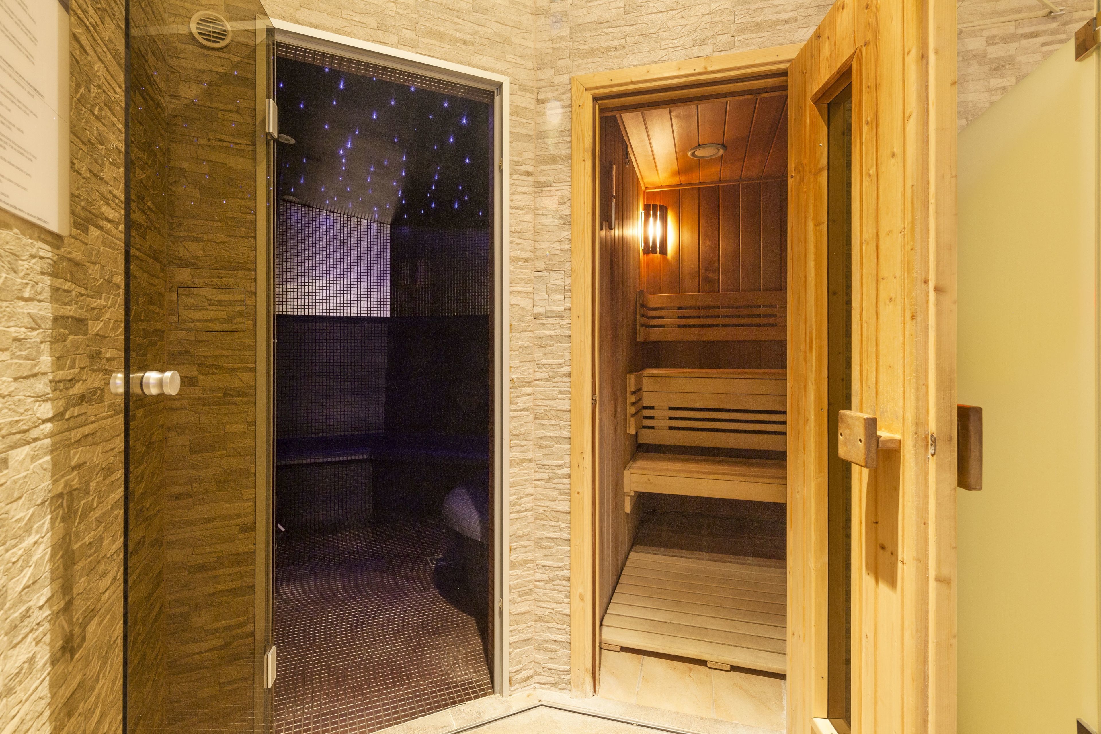 A sauna room with a wooden bench, a glass door with a starry night view, and a stone wall.