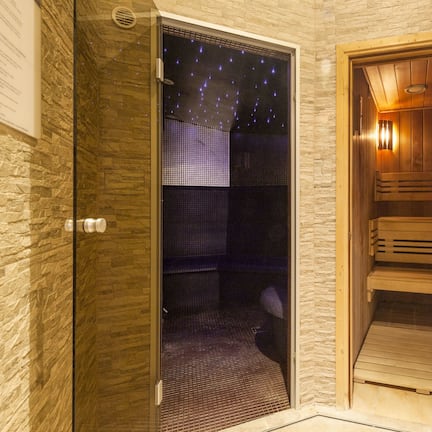 A sauna room with a wooden bench, a glass door with a starry night view, and a stone wall.