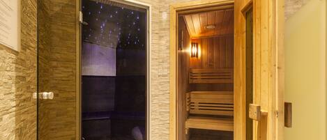 Uma sala de sauna com banco de madeira, porta de vidro e vista para uma noite estrelada, além de uma parede de pedra.
