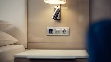 Een moderne hotelkamer met nachtkastje, lamp en een stopcontact op de muur.