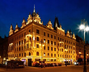 Un edificio histórico con varios pisos, detalles arquitectónicos ornamentados y señalización iluminada que indica diferentes establecimientos como restaurantes y un casino.
