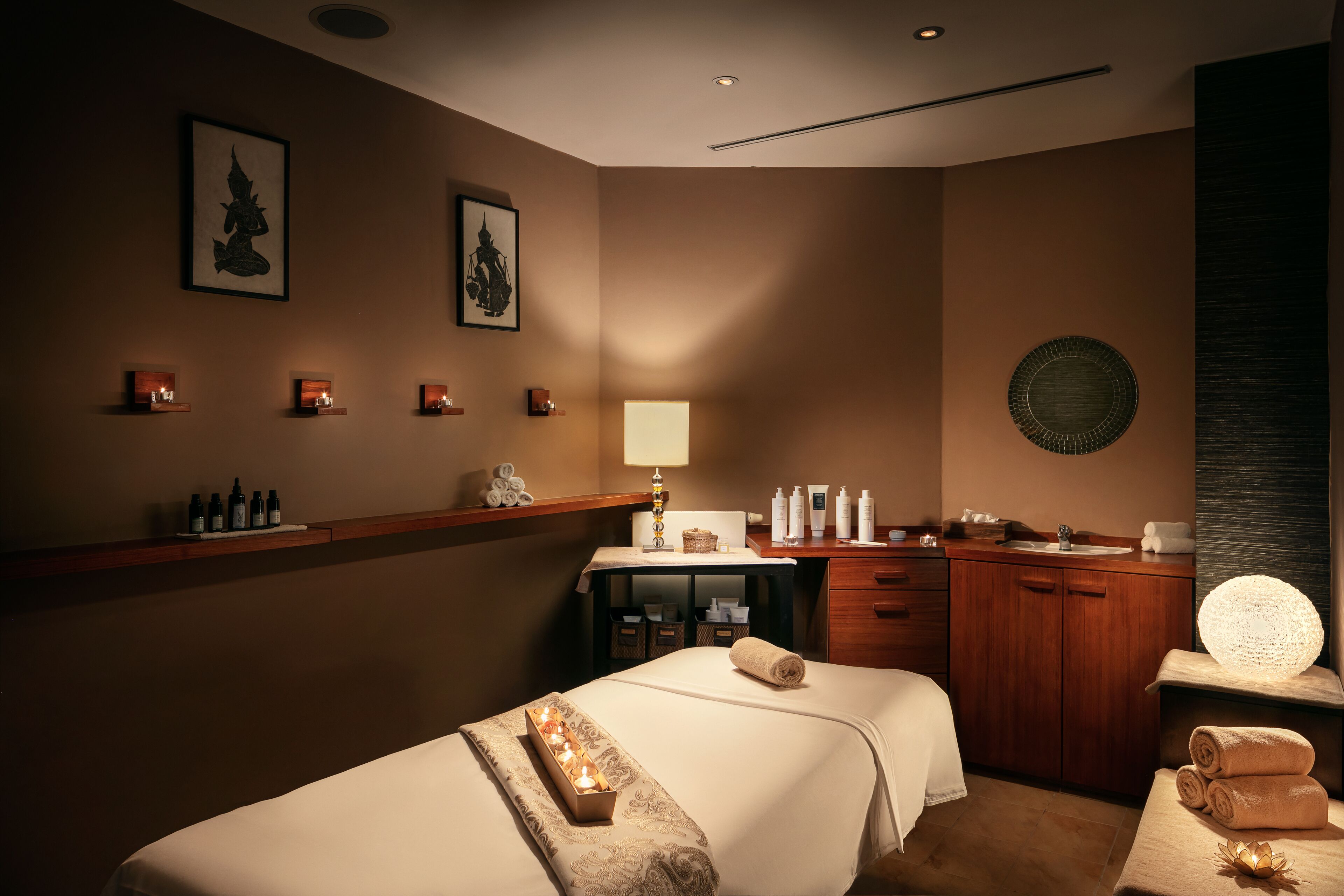 A hotel room with two beds, a vanity with toiletries, a small desk, and wall-mounted artwork.