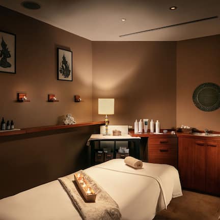 A hotel room with two beds, a vanity with toiletries, a small desk, and wall-mounted artwork.