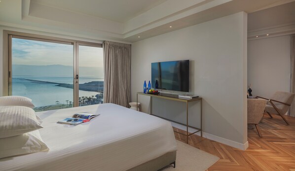 A hotel room with a large bed, a TV on a stand, a chair, and a view of the sea. - Brown Dead Sea by Brown Hotels (Tamar)