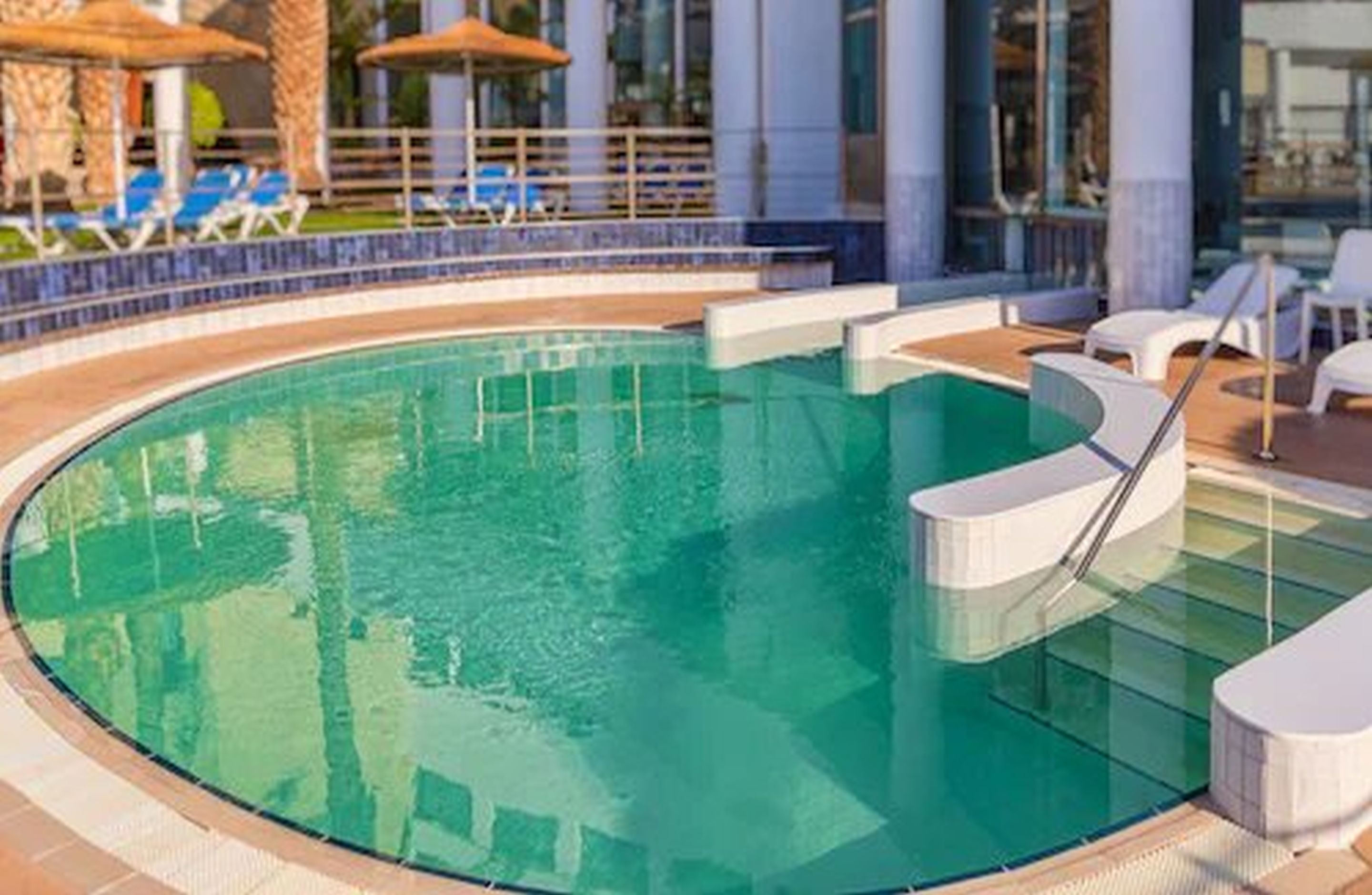 Una piscina rodona amb aigua cristal·lina, envoltada de gandules blanques i ombrelles.