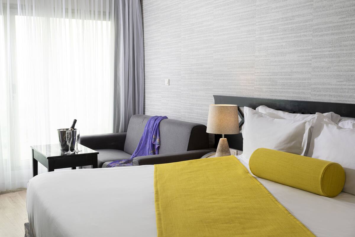 A hotel room with a bed, a nightstand, a lamp, a chair, and a window with curtains.