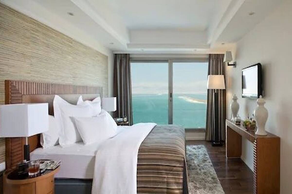 A hotel room with a large bed, a nightstand, a TV, and a view of the ocean.