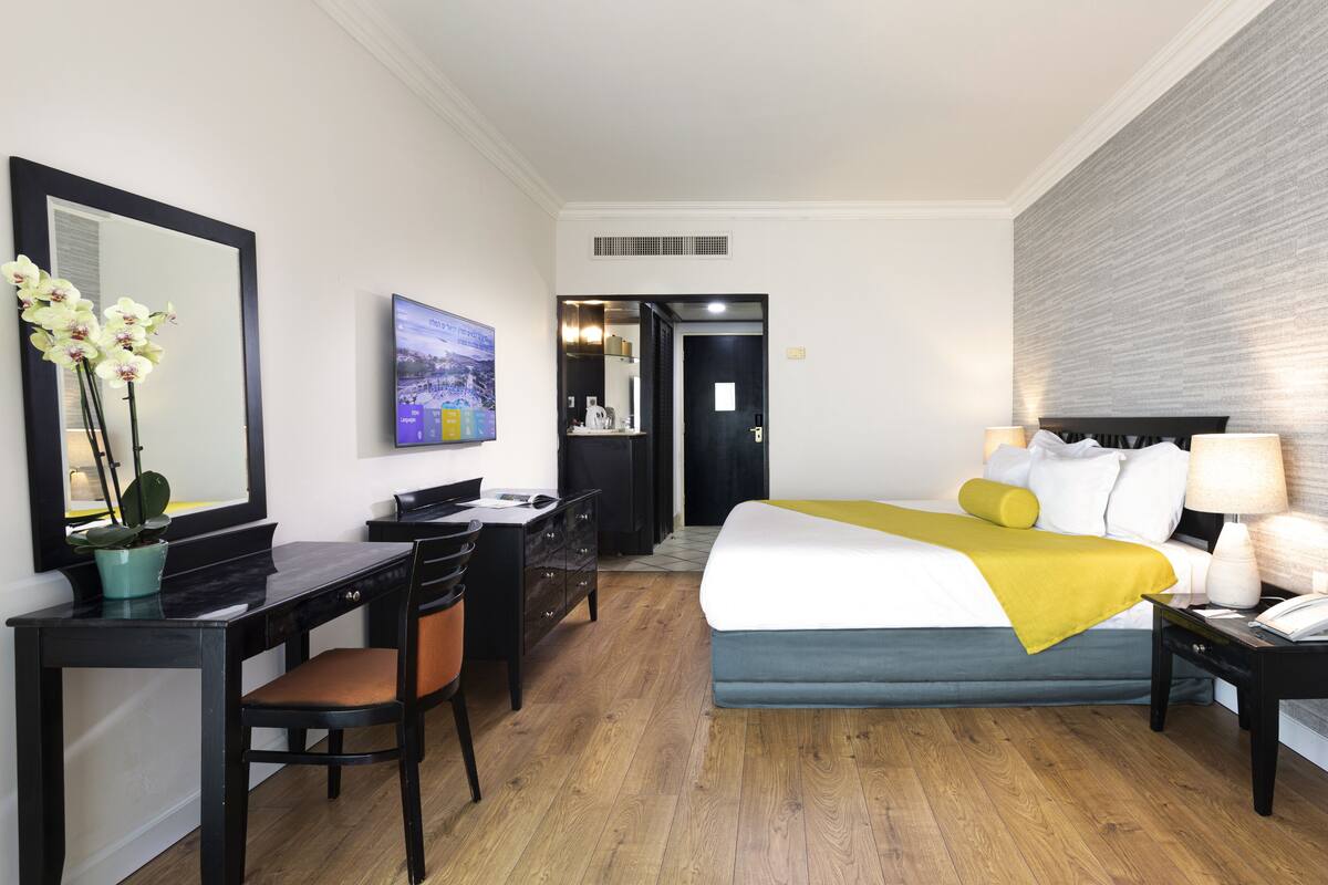 A hotel room with a bed, desk, chair, and a large mirror.