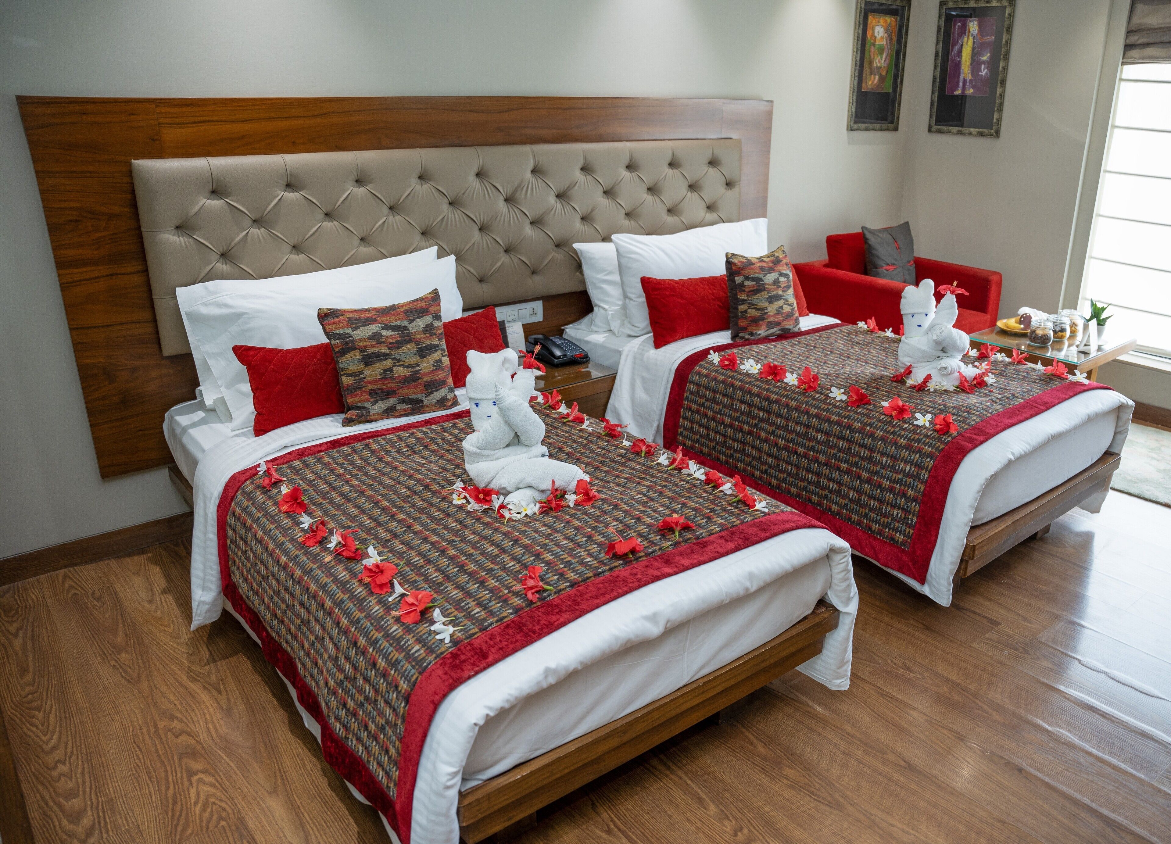 Une chambre d’hôtel avec deux lits, chacun doté d’une tête de lit capitonnée, de linge de lit blanc et d’éléments décoratifs rouges.