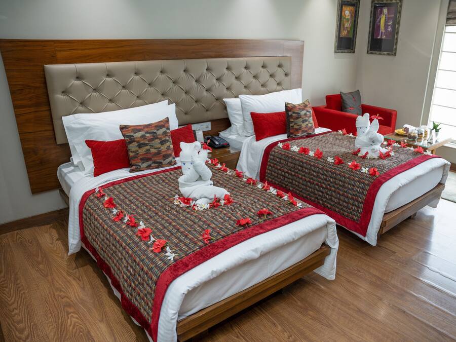 Une chambre d’hôtel avec deux lits, chacun doté d’une tête de lit capitonnée, de linge de lit blanc et d’éléments décoratifs rouges.