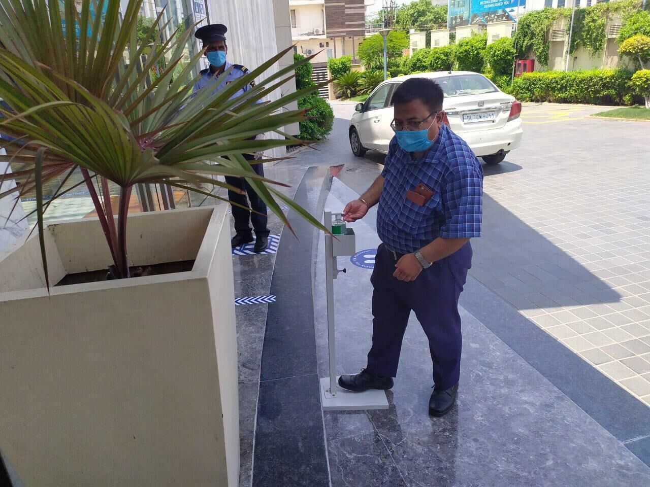 A man standing on a tiled floor with a plant beside him, a car parked in the background, and a building with a white facade.