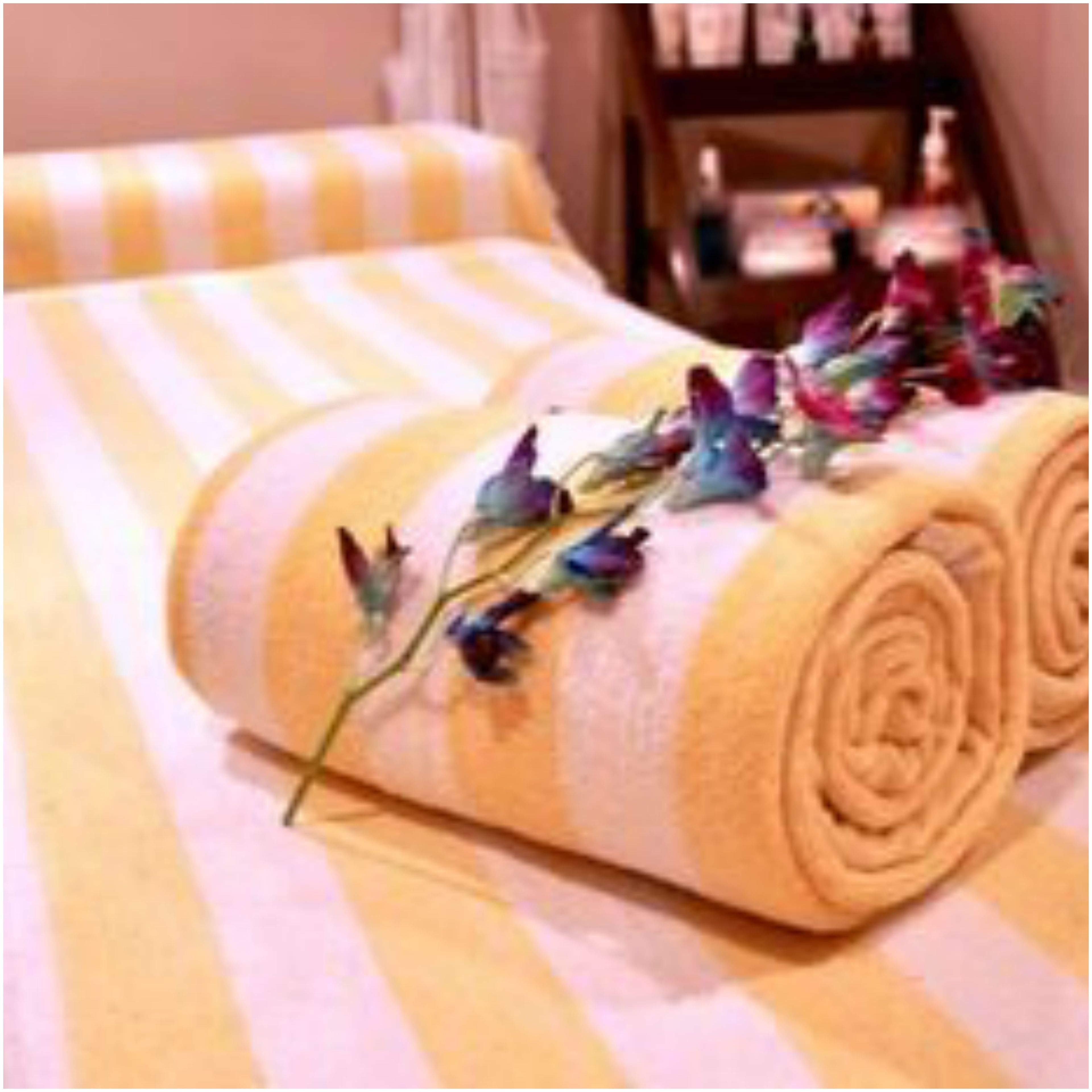 A neatly rolled towel with floral decorations on a striped bedspread.