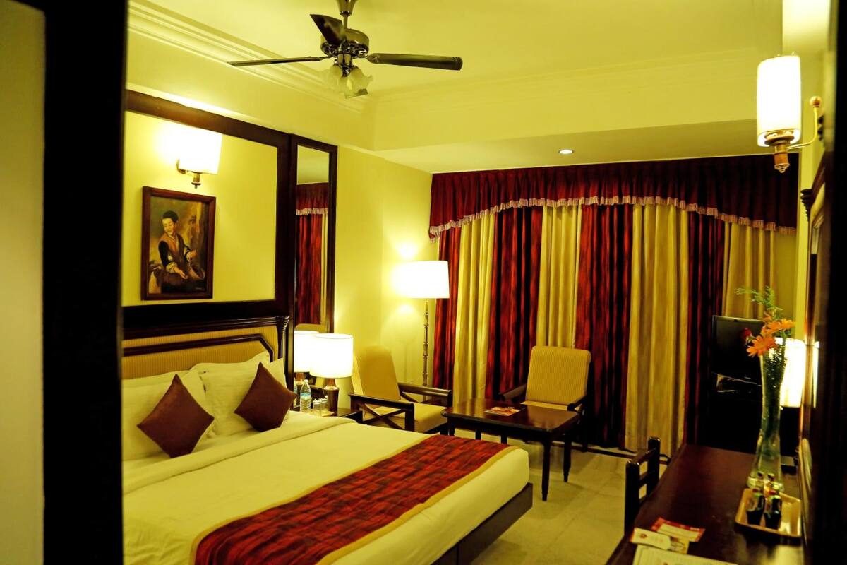 A hotel room with a bed, bedside lamps, a desk, a chair, a television, and a window with curtains.