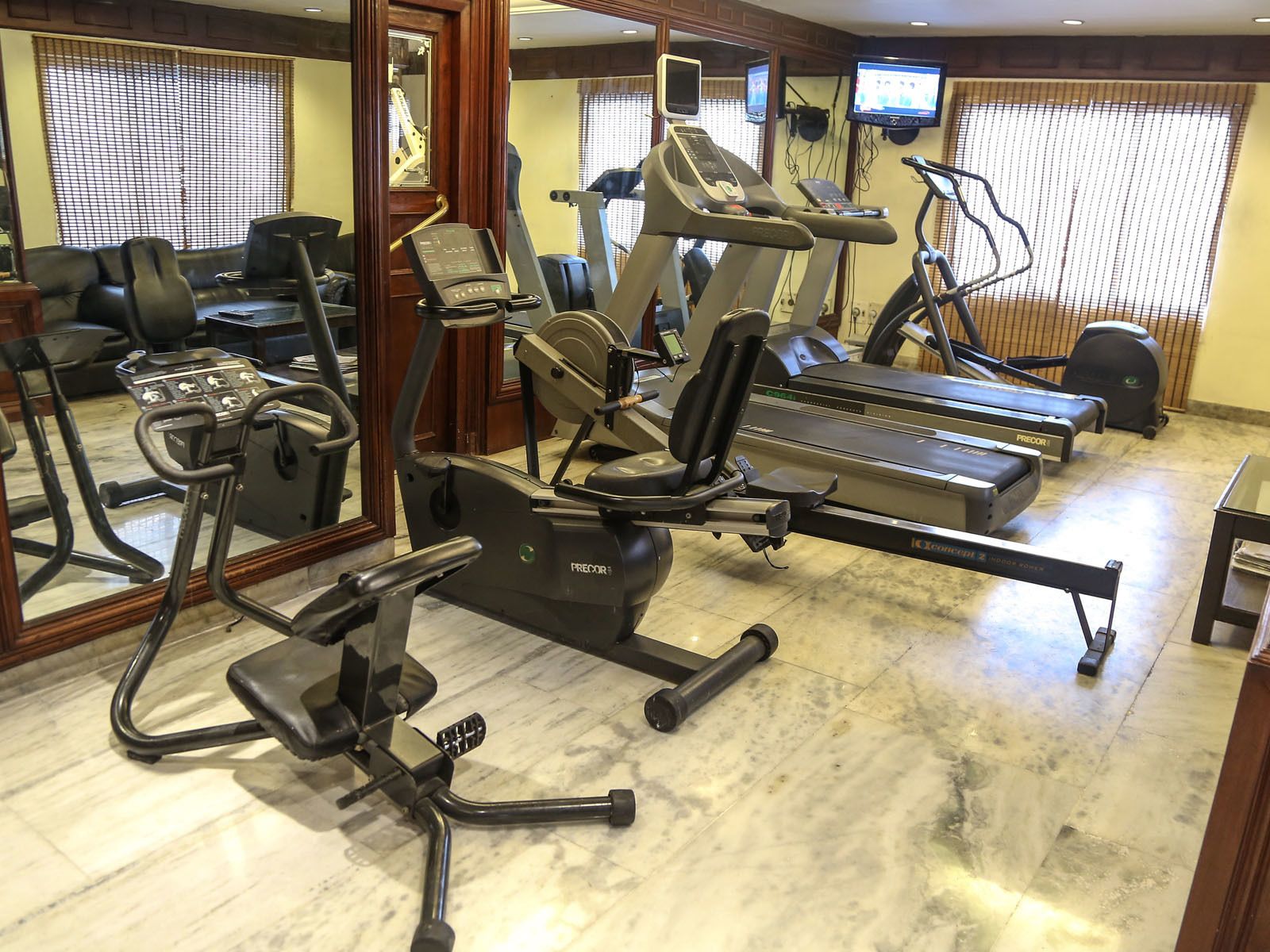 A gym with various cardio machines, a mirrored wall, and a television on the wall.