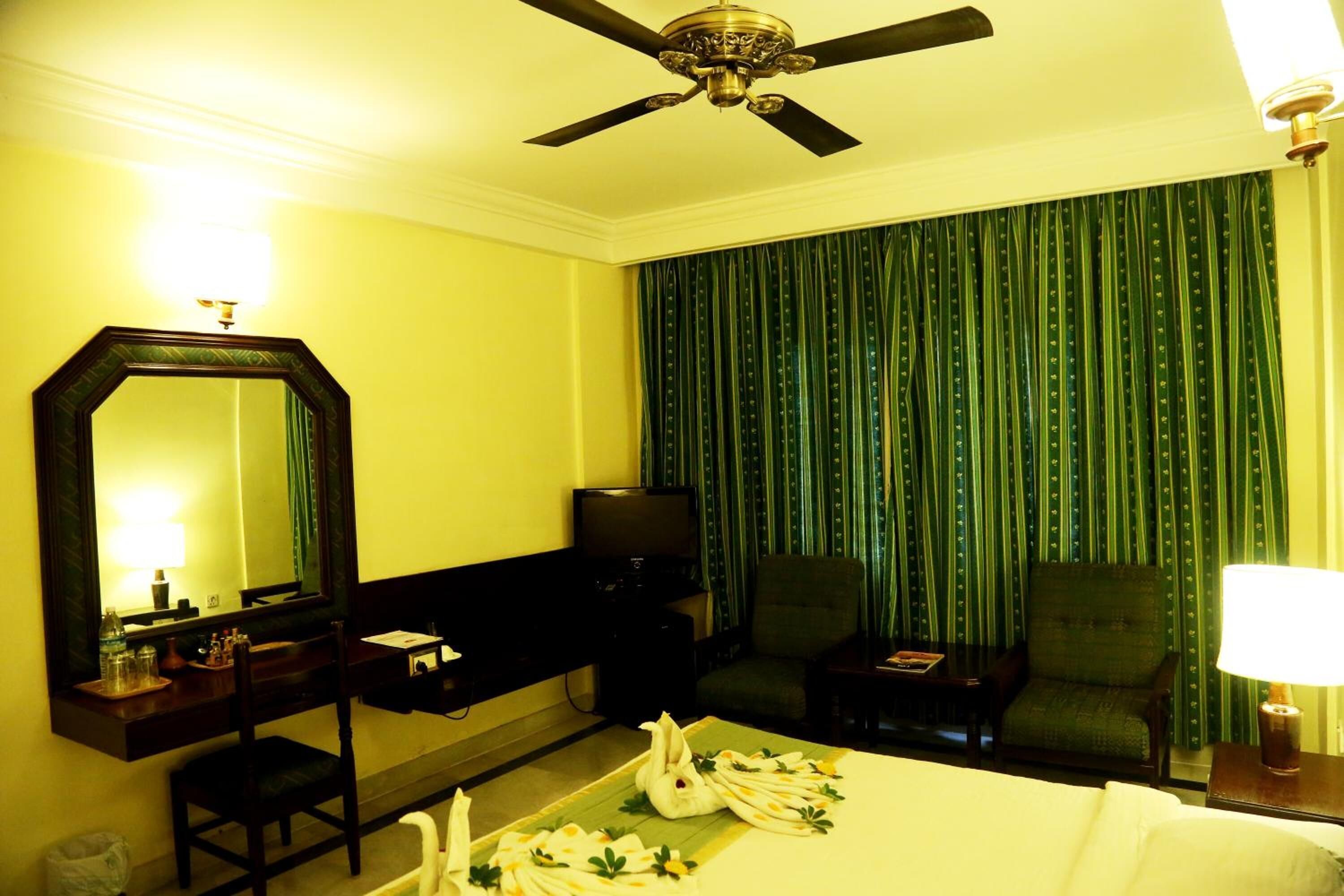 Una habitación de hotel con cama, escritorio, silla, televisor y ventilador de techo.