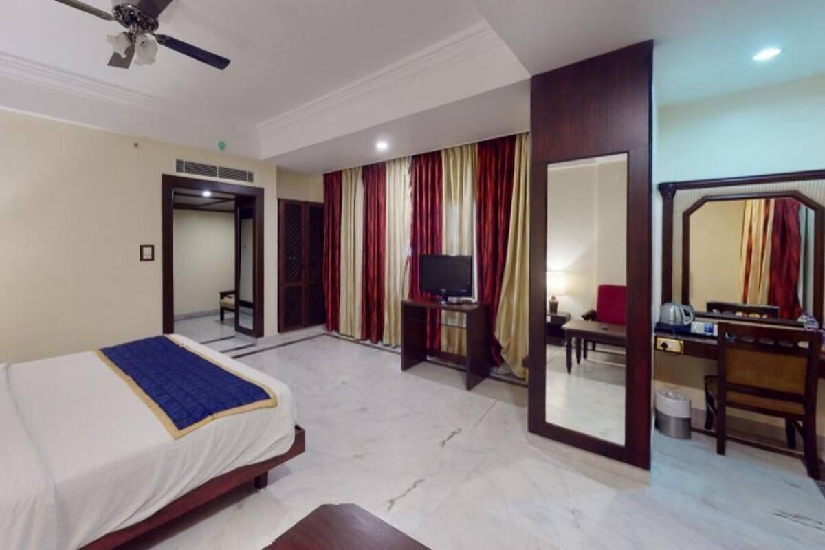 A hotel room with a bed, a desk, a television, a mirror, and a ceiling fan.