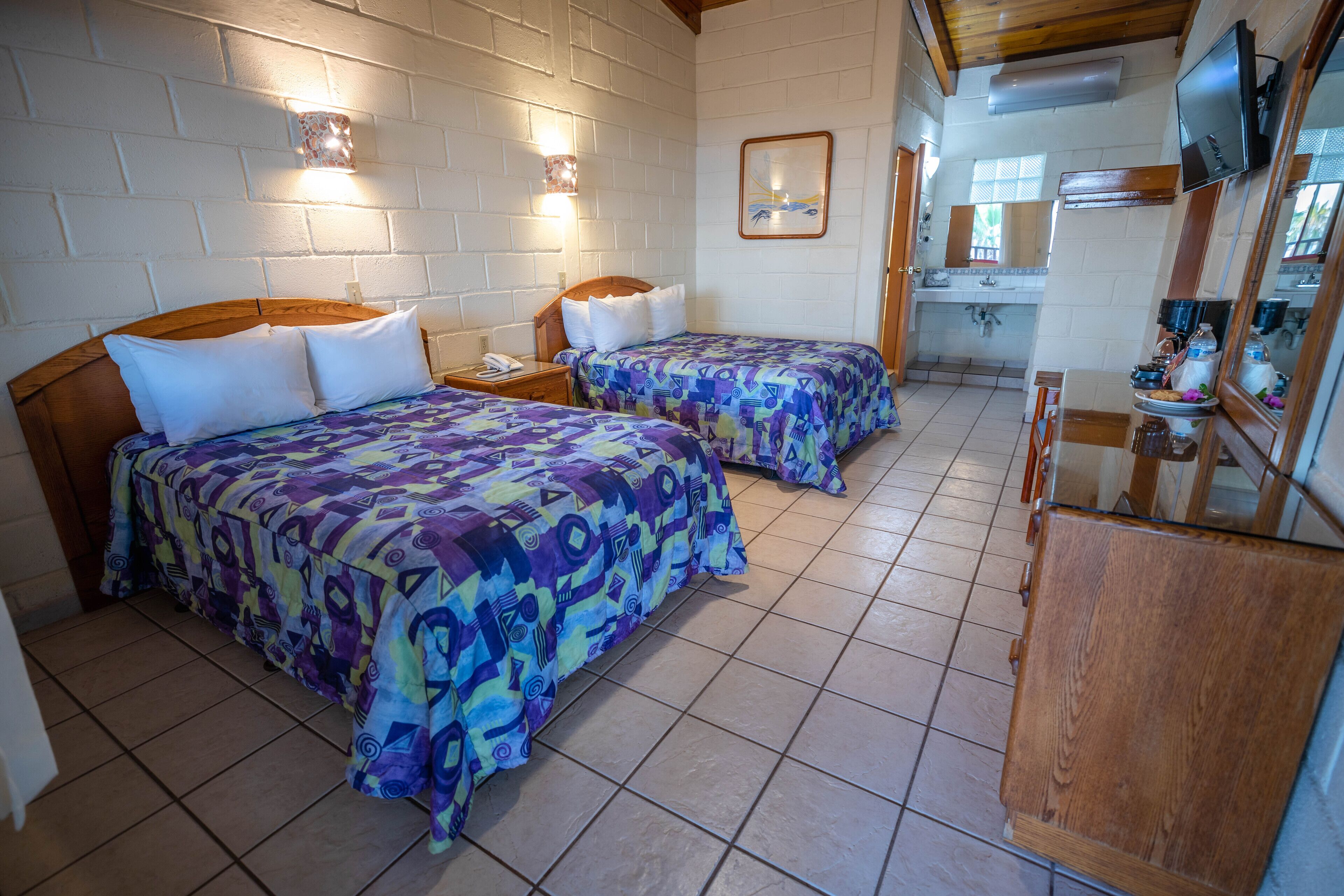 Een kamer met twee bedden, een houten hoofdbord, een nachtkastje, een klein tafeltje, een spiegel en een televisie.