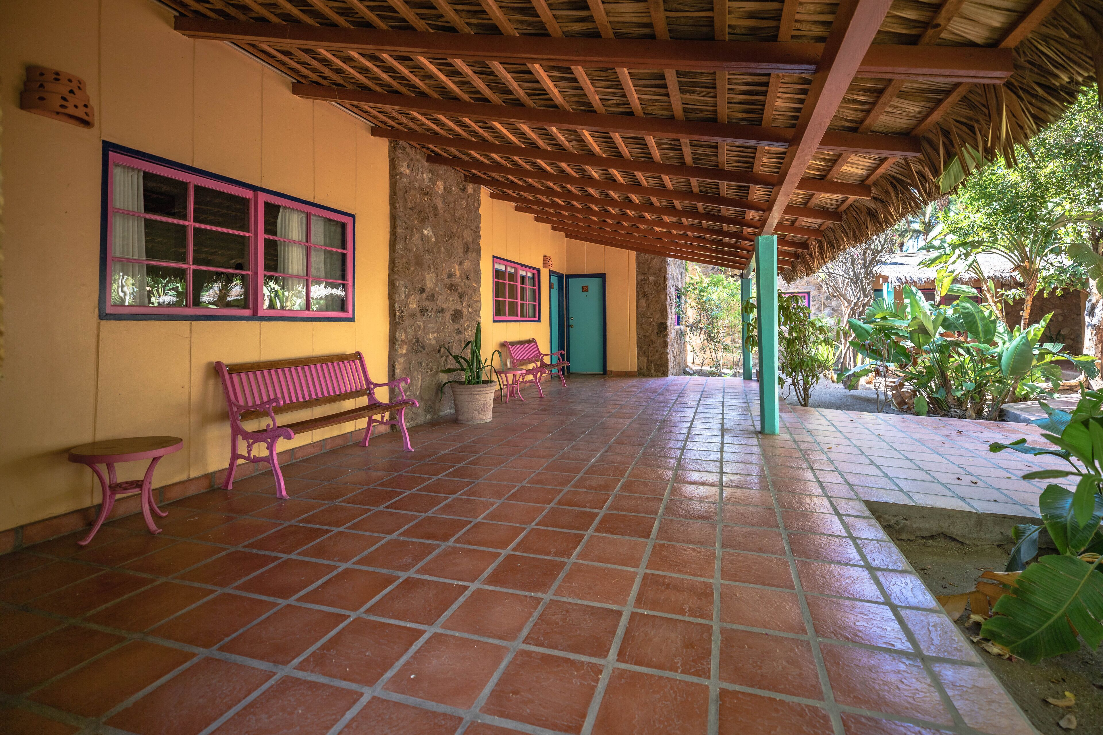A covered patio area with tiled flooring, benches, and potted plants.
