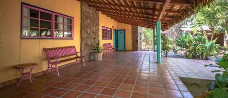 A covered patio area with tiled flooring, benches, and potted plants.
