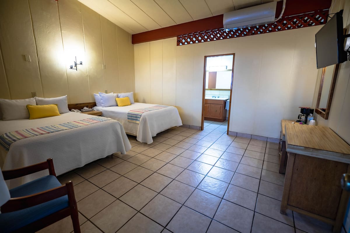 A hotel room with two beds, a desk, a chair, and a bathroom visible through a doorway.
