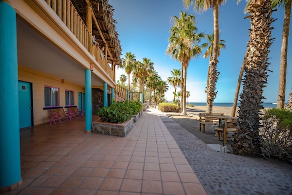 A hotel corridor with a tiled floor, wooden benches, and palm trees. - Hotel Oasis (Loreto)