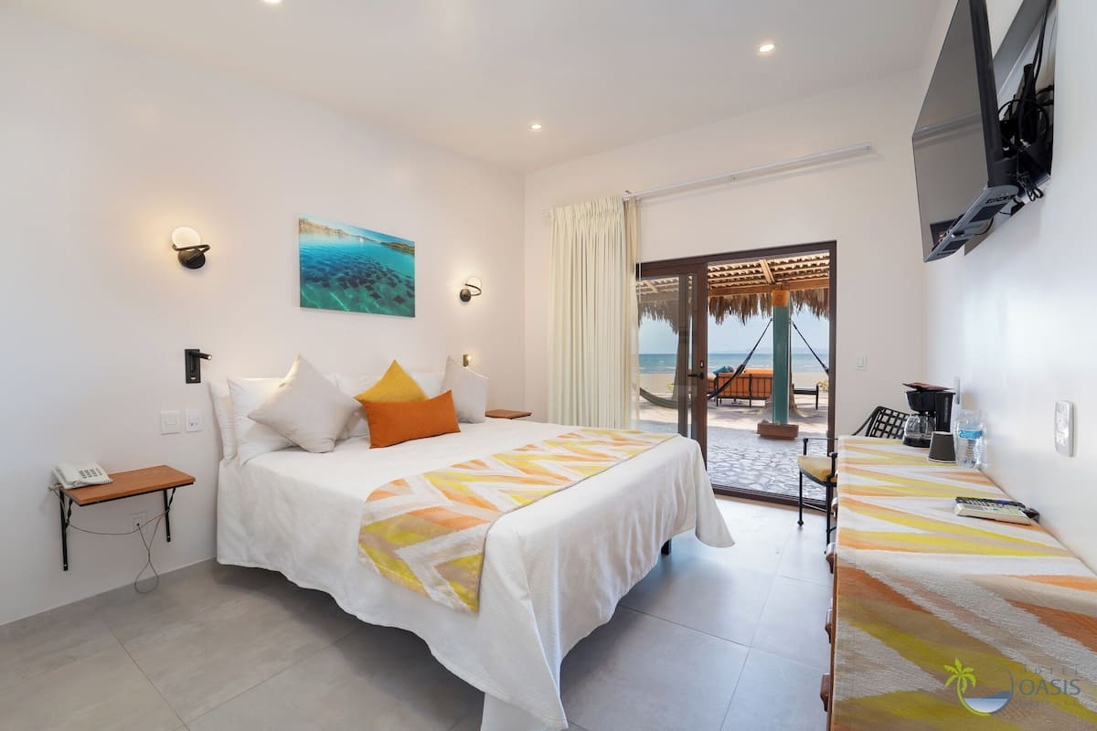 A hotel room with a bed, a desk with a chair, a TV, and a view of the sea through a glass door.