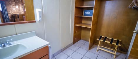 Un baño con lavamanos blanco, estantes de madera, un espejo y una puerta de madera.